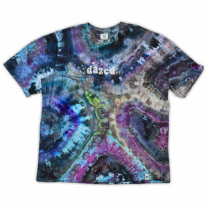 The vibrant patterns of this tie-dye t-shirt are reminiscent of a sliced geode, with bands of blue, purple, and green that encircle the 'dazed' text, which glistens like a quartz inscription.