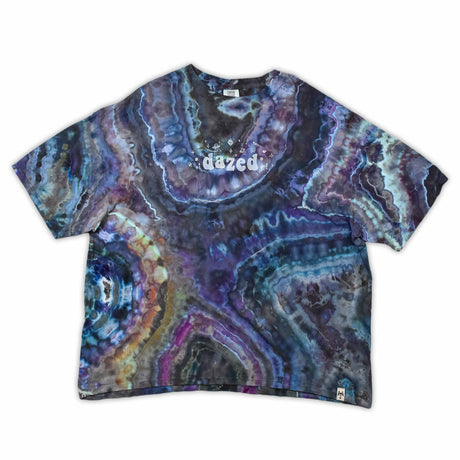 The vibrant patterns of this tie-dye t-shirt are reminiscent of a sliced geode, with bands of blue, purple, and green that encircle the 'dazed' text, which glistens like a quartz inscription.