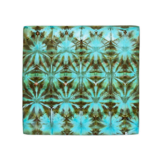 A handcrafted bandana combining the art of ice dyeing with itajime folding, creating a kaleidoscope of cool blues and greens with touches of rustic brown.