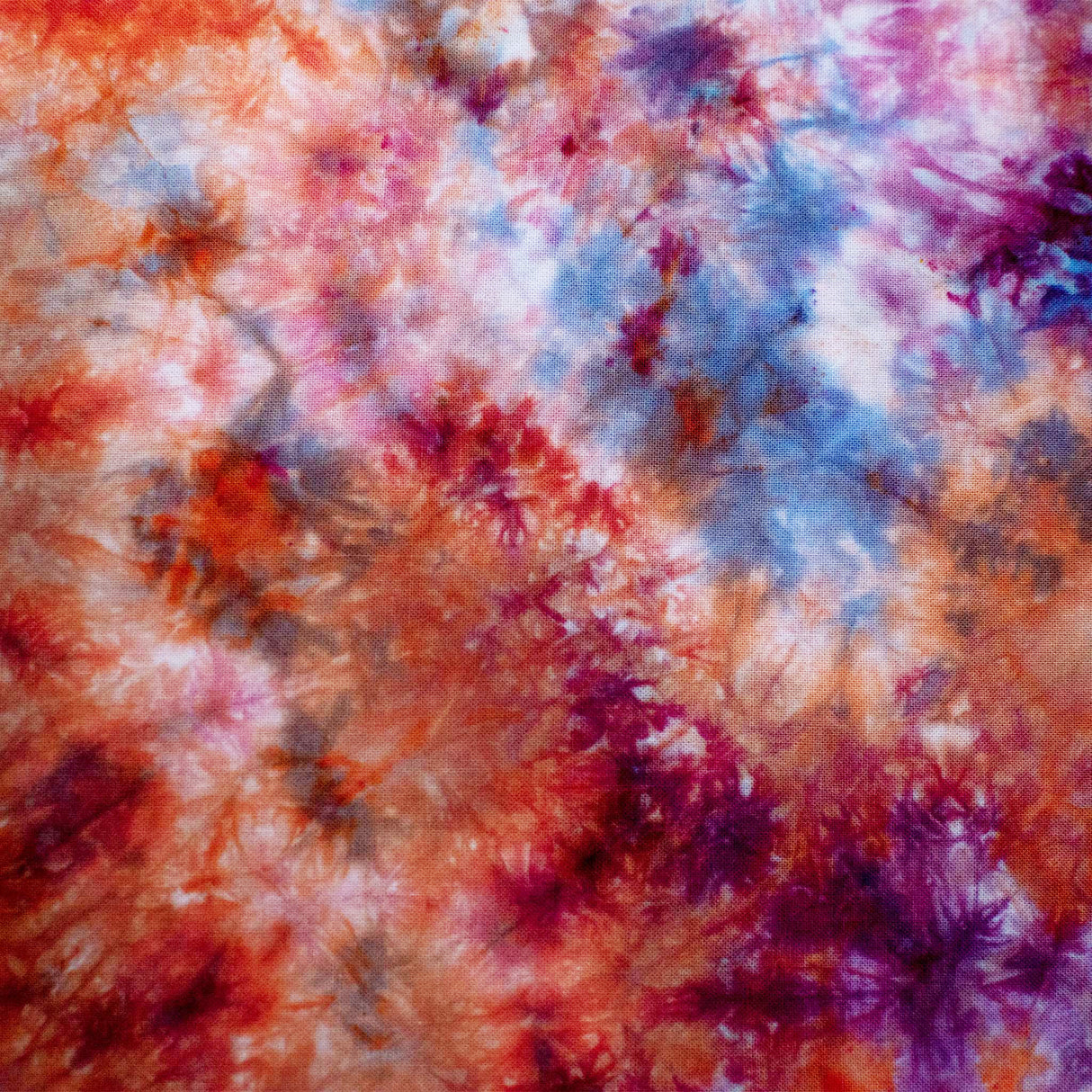 A hand-dyed bandana characterized by its ice-dyed effect, showcasing a storm of warm and cool colors, with prominent shades of rust and lilac resembling a nebula.