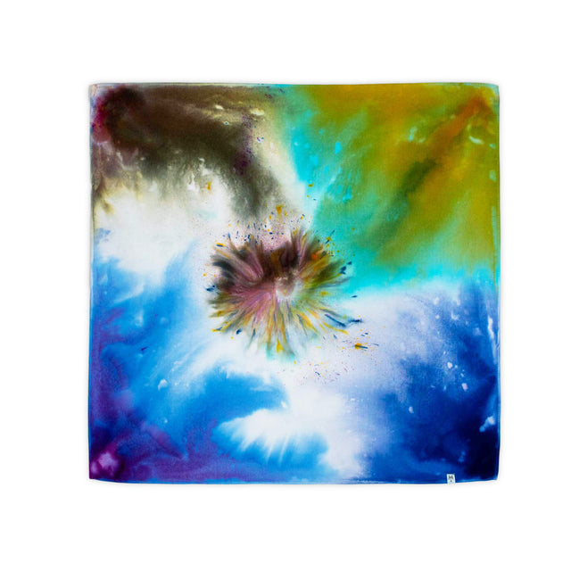 The bandana features a dramatic ice dye effect, with a starburst of amber and violet hues set amidst a serene blue and green field, resembling a galaxy.