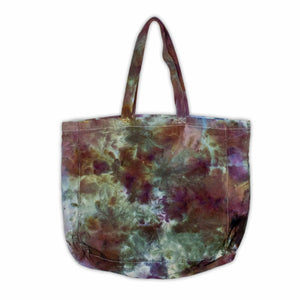 A sturdy canvas tote bag featuring an abstract ice-dyed pattern in earthy tones of green, brown, and purple, with the white logo "Woof Dyes" prominently displayed.