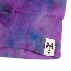 A tie-dye sweatshirt showcases a vibrant pattern of purples and blues, with colors merging fluidly. The ribbed cuffs and hem indicate a cozy and comfortable design.