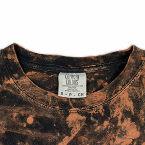 A stylish bleached t-shirt makes a statement with the 'Woof Dyes' logo, amidst a mottled backdrop of blacks and browns for a rugged look.